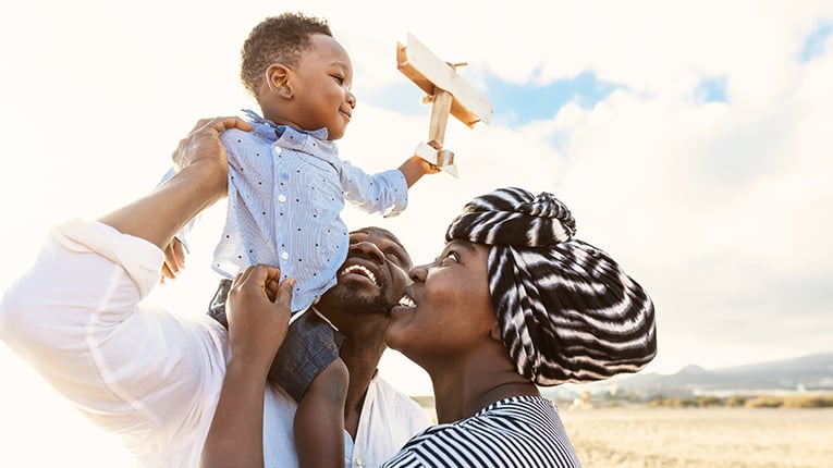 Happy African American family having fun holding baby smiling on the beach