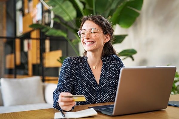 Credit cards can help you enjoy life, cover the unexpected, and bring a smile to your face like this woman shopping on her laptop.